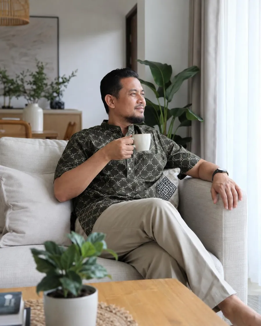 Seorang lelaki duduk tenang di ruang tamu sambil minum teh pada waktu pagi